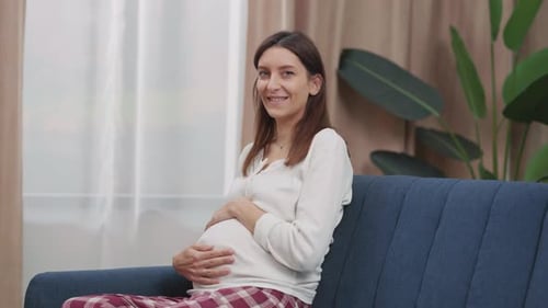 Caucasian Pregnant Woman Smiling Cheerfully at Camera Gently Hugging Her Baby Belly and Sitting on