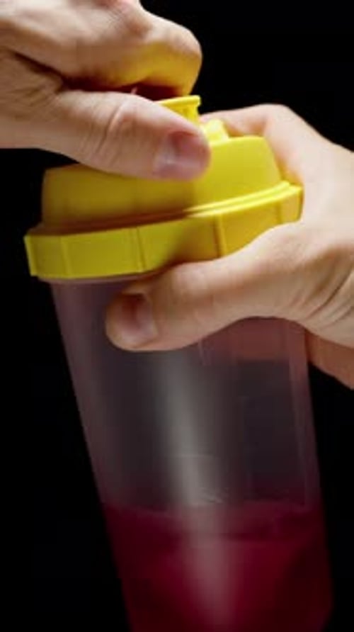 Vertical video. Mixing a Sports Drink in a Shaker and Bringing the Cup Close to Drink. Slow-Motion