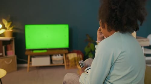 Girl with Remote Control Sitting in front of TV Set with Chroma Key Screen