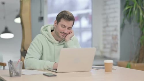 Müder junger Mann schläft bei der Arbeit am Laptop