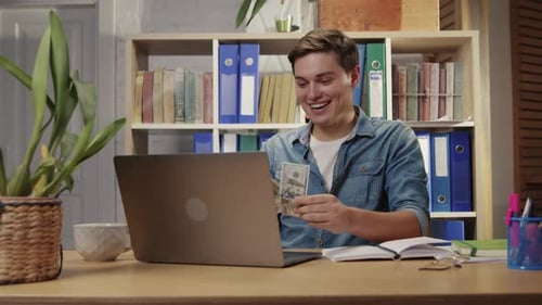 Joven empleado que obtiene ganancias en línea que saca dinero de la computadora disfruta de manera fácil y rentable