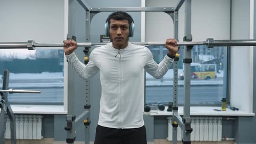 Young Man Squatting with Barbell on Shoulder in Gym Near Window with Car Outside