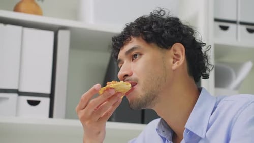 Asian young businessman eating homemade pizza while working in office.