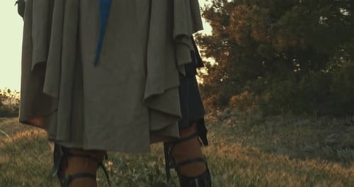 A Man in a Medieval Knight Costume Stands in a Forest with a Sword Above His Head Against the