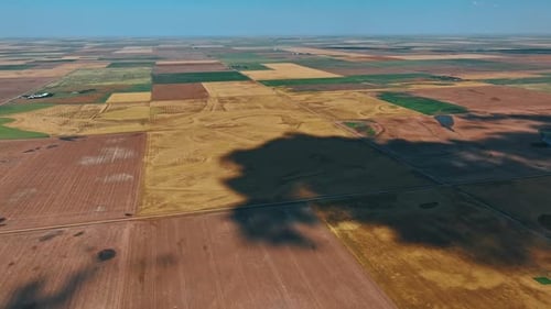 Big shadow from cloud spreads by the ground. Vast territory divided into the fields for agriculture.
