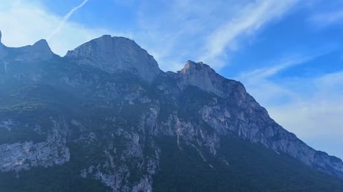 Wispy clouds are slowly moving over a mountain peak on a sunny day