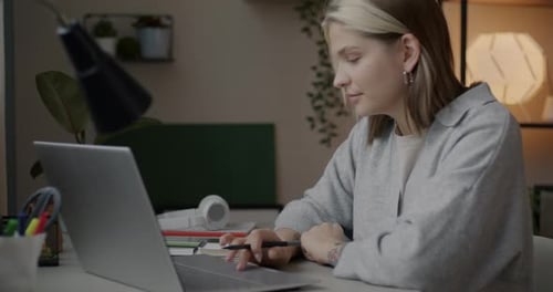 Woman Works on Laptop and Writes in Notebook