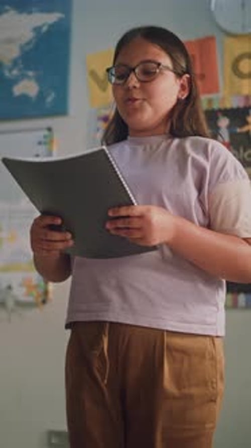 Primary School Girl Holding Notebook Showcasing Knowledge of Geography in Front of Classmates