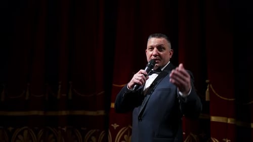 Actor with microphone announces performance before auditorium. Theater curtains background.