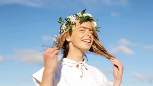 Smiling young woman in flower wreath shaking head enjoying summer sun outdoors