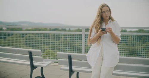 Woman Using Smartphone on Rooftop Near Park Benches
