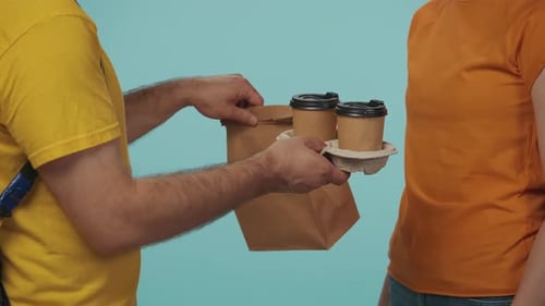 Gros plan : un livreur en uniforme jaune donne à une cliente sa commande de café et de nourriture