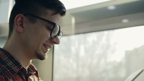Young Man Smiling Using Tablet by Sunny Window