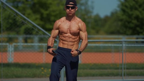 Young Shirtless Man Showing Off Big Biceps and Abs While Standing on an Outdoor Sports Field with