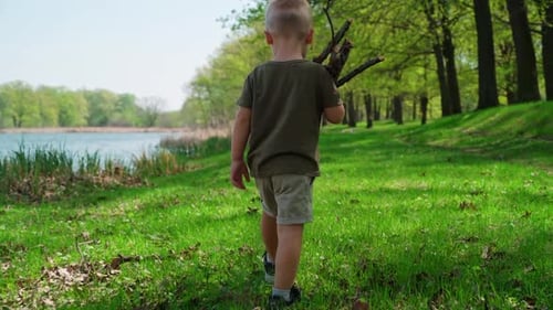 The camera follows a small boy walking across the lawn by the river.