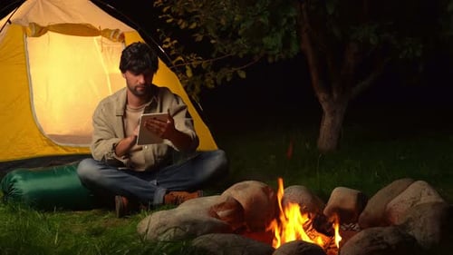 Young Adult Using Tablet by Campfire at Night