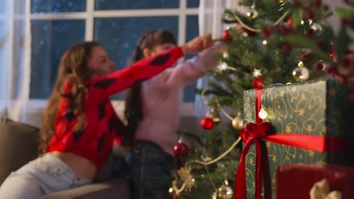 Caucasian mother and kid daughter feeling happy decorating Christmas tree in house.