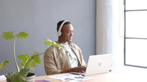 Using laptop and wearing headphones, man having video conference in office