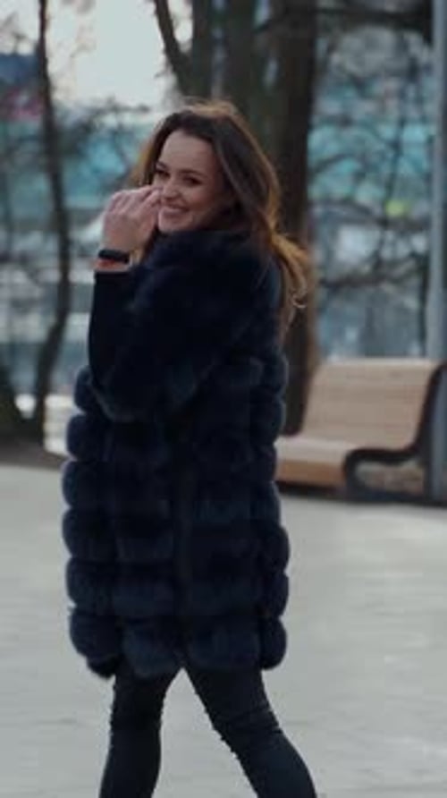 Happy model walking. Beautiful young woman in stylish fur coat walks in the park.