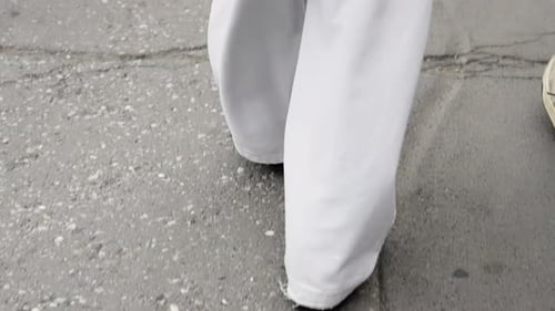 Closeup View of a Person Walking on a Textured Urban Sidewalk Showing Loose White Wideleg Trousers