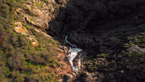 Flowing creek cascades down rocky cliffs in a tranquil landscape during golden hour sunlight