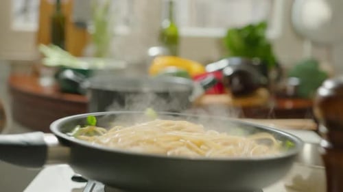 Person Cooking Pasta with Vegetables in Kitchen