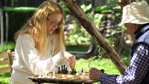 Young Woman Playing Chess with Senior Man Outdoors