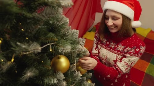 Woman Decorates Christmas Tree with Golden Ornaments