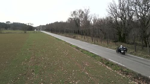 Panoramic Crop Field Next to a Narrow Road on Which a Traveling Motorcyclist Travels on a Gray Day