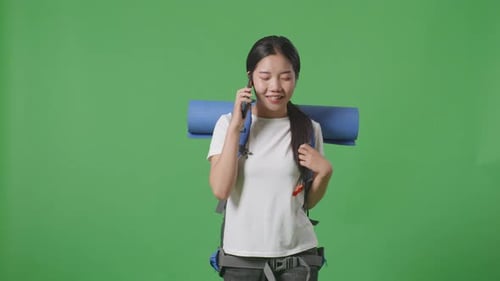 Asian Female Hiker Talking On Smartphone And Looking Around While Walking On Green Screen