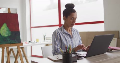 Video of biracial female designer working on laptop in studio