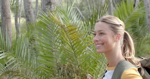 A young Caucasian woman smiles while exploring a lush outdoor setting with copy space