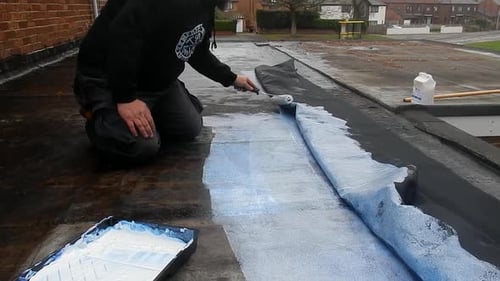 Man Coating Roof with Roller in Urban Setting