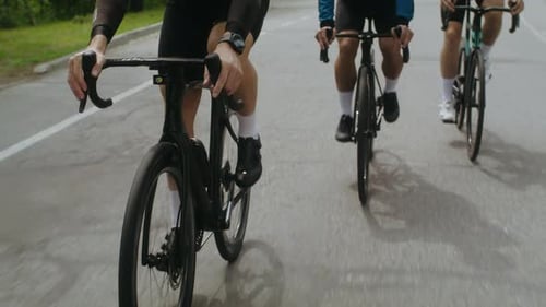 Cyclists with Muscular Legs Ride Bicycles Along Asphalt Road