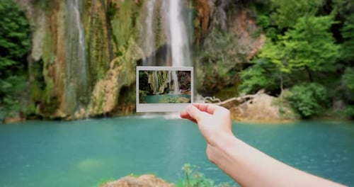 4k video footage of a unrecognizable woman holding a polaroid infront of a waterfall