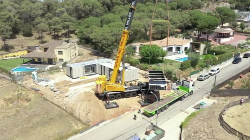 Kran, der ein modernes modulares Haus vom LKW auf die Immobilienbaustelle hebt, Luftorbit l