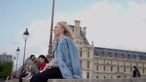 Vídeo em câmera lenta de uma jovem mulher com uma jaqueta jeans sentada perto do Louvre em Paris Vídeo