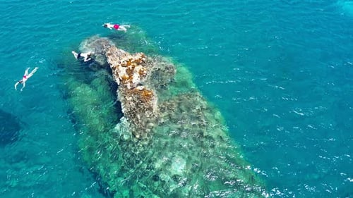 top aerial view of young tourists swimming around a rock in the mediterranean sea with diving mask