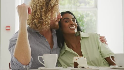 Happy diverse couple with coffee embracing and talking in cafe