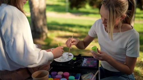 Closeup of Two Girls Mixing Paint on a Palette During a Creative Outdoor Art Session in a Park