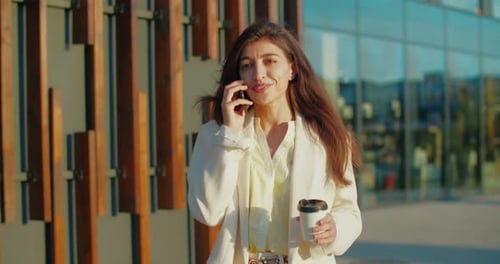 Smiling Woman on Phone Call Outdoors with Coffee