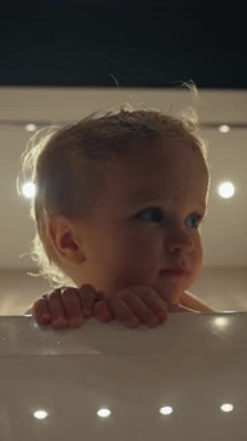 Vertical d'un bambin blond assis dans la baignoire contre des lumières vives au plafond