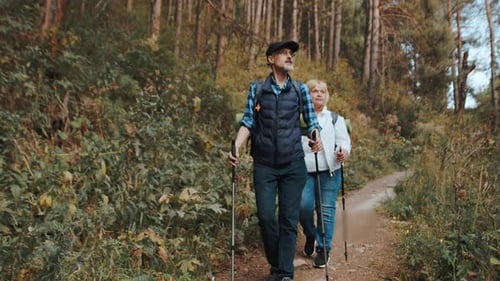 Caucasian Tourist with a Backpack and Hiking Sticks Walking with a Woman on a Forest Trail and