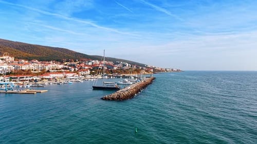 Sailboats are moored at the harbor as a coastal town is visible along the shore under