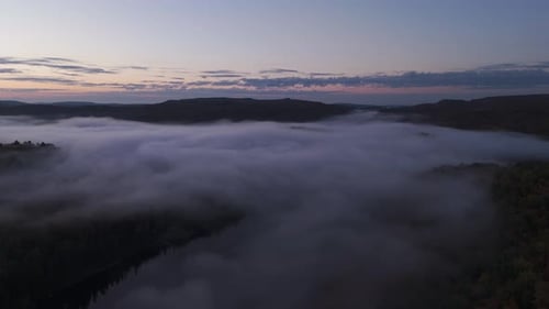 drone above sea of clouds in a foggy misty landscape at sunset , aerial of forest in nature
