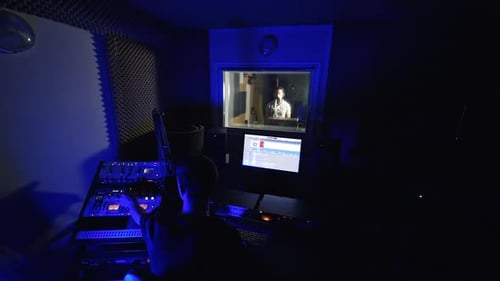 Music engineer sitting in dark studio in front of sound board.