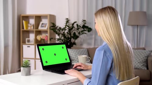 Woman at home having a video call on laptop computer with green chroma key screen