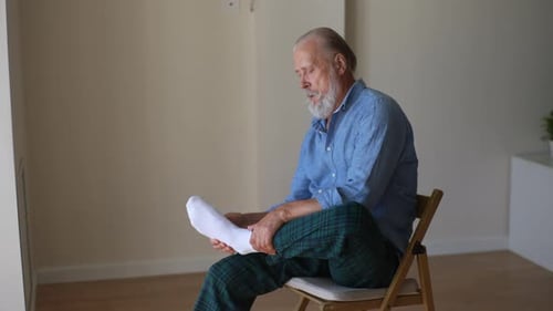 Senior Man Putting on Sock in a Bright Room