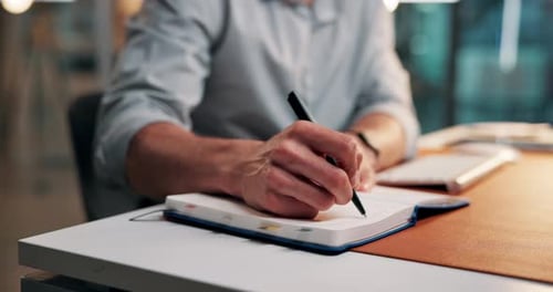 Man Writing in Notebook at Desk in Office