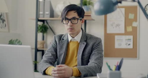 Slow Motion Portrait of Handsome Asian Guy Office Worker Looking at Camera Sitting at Desk